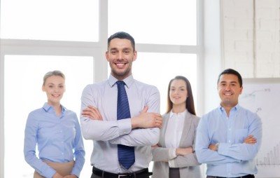 smiling handsome businessman with crossed hands and team in office